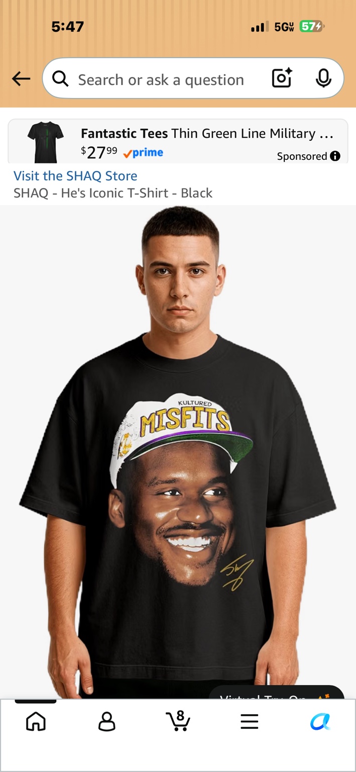 Model wearing a black SHAQ He's Iconic T-shirt with a large Shaquille O'Neal portrait and gold signature graphic